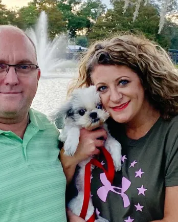 small white dog held by two happy adults